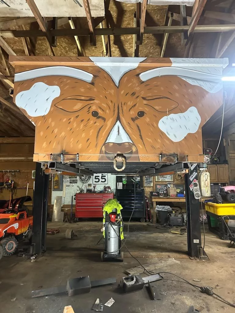 ten cubic yard roll off dumpster in barn on risers. it is painted with to look like a longhorn bull